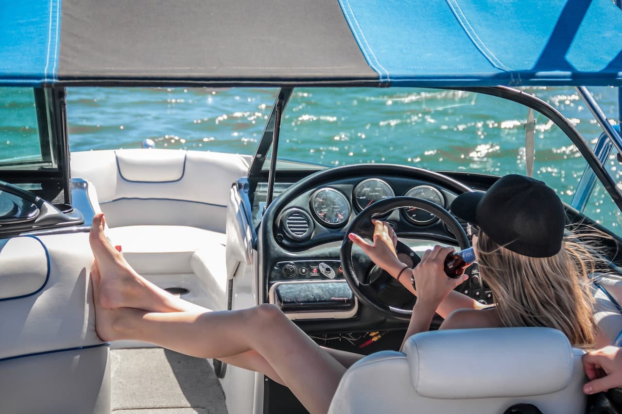 women wearing black cap holding steering wheel in speedboat