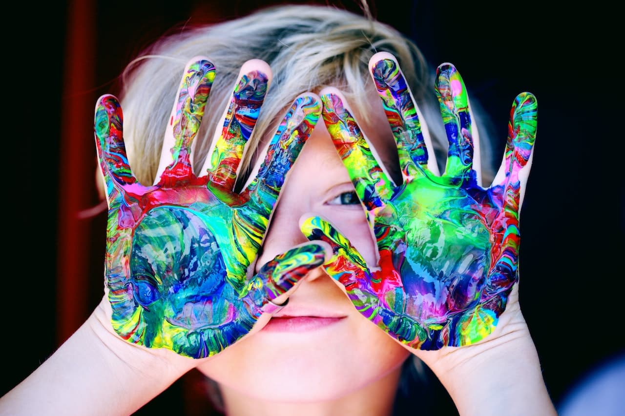 a child with multicolour finger paint on hands