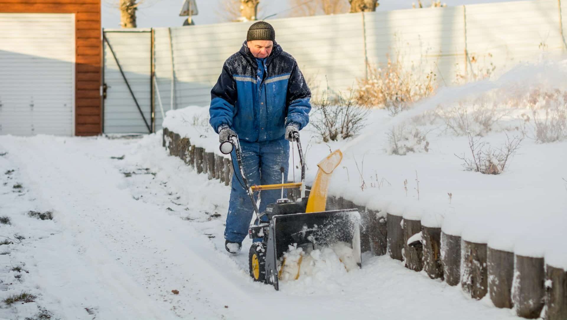 A man using a snowblower to clear snow off of a walkway, representing snow removal and business liability in Alberta