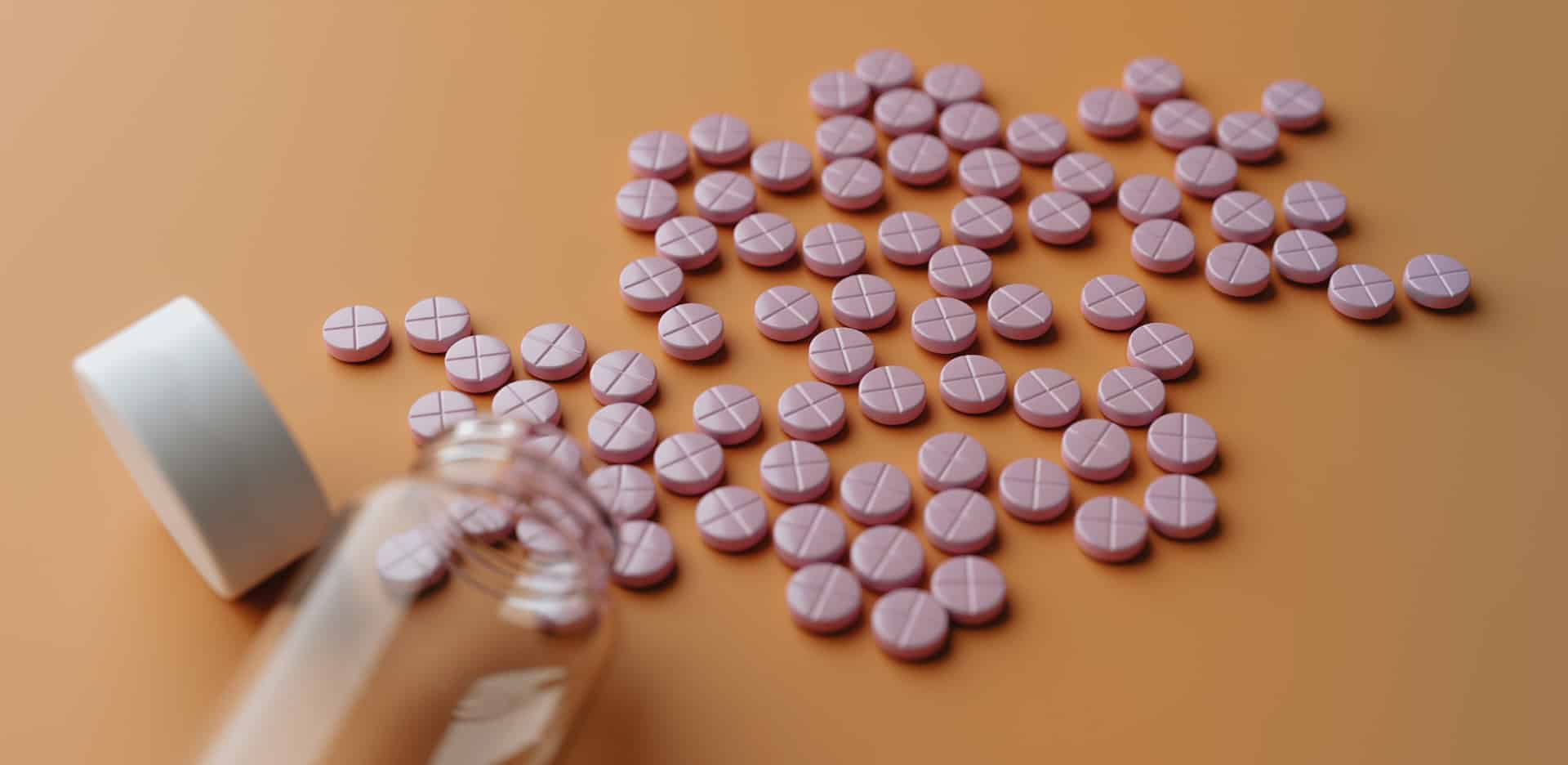 Pink pills spilled over a table from a clear pill bottle, representing opioid addiction.