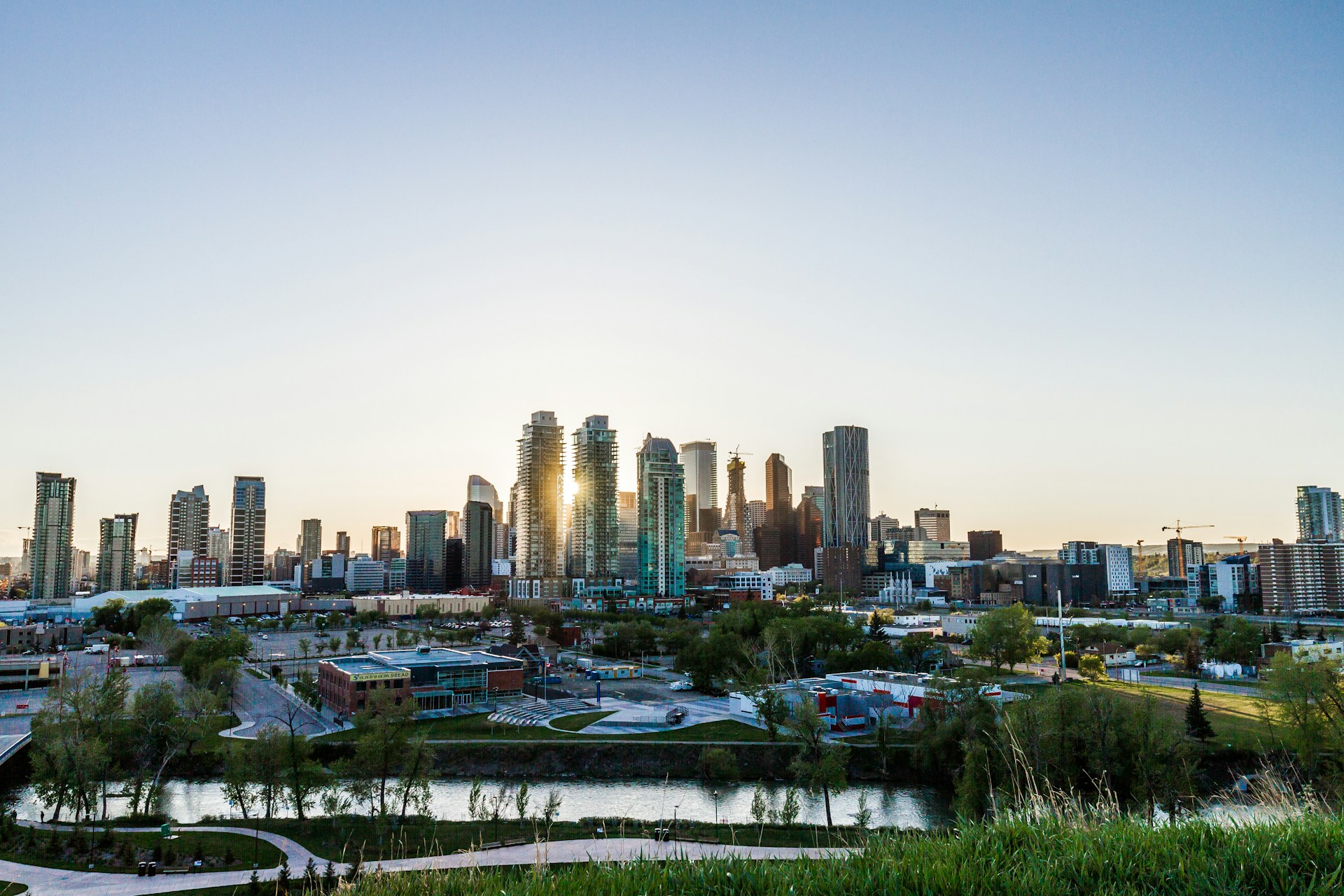 The Calgary skyline with the sun rising between the buildings under a cloudless blue sky, representing best law firms Canada.