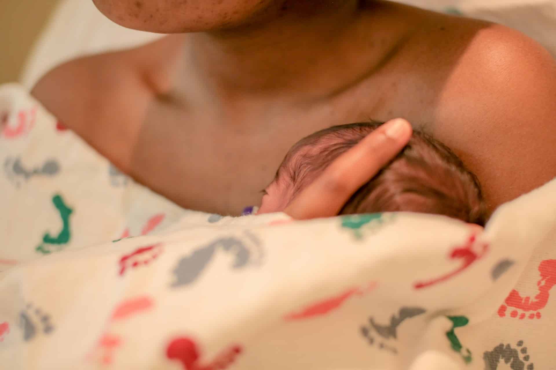 Close-up of a newborn baby's head resting skin-to-skin on the chest of a parent, wrapped in a hospital blanket, illustrating early bonding and recovery in the immediate postpartum period, with potential context for conditions like Maternal sepsis.