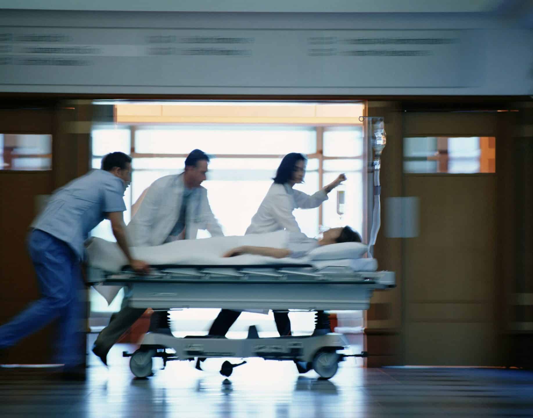 A blurred image of two doctors and a nurse running down a hospital hallway while pushing a patient on a gurney, representing ER negligence in Alberta.