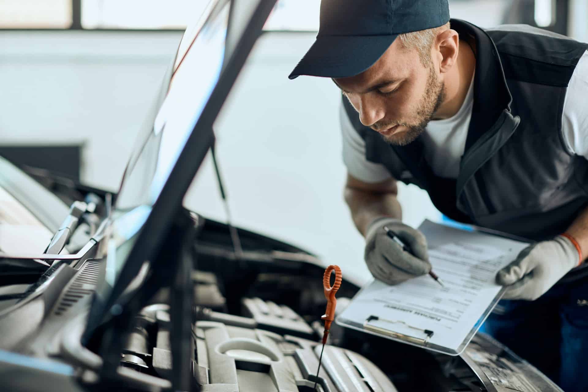 A mechanic inspects a car's engine while making notes on a clipboard, representing negligent maintenance at car dealerships.