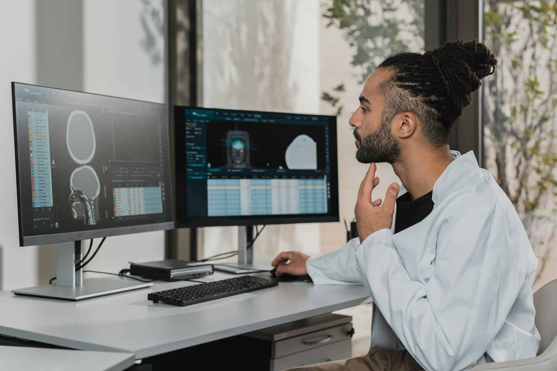 A radiologist reviews scan images on two computer screens on the desk he is sitting at, representing missed cancer diagnosis.