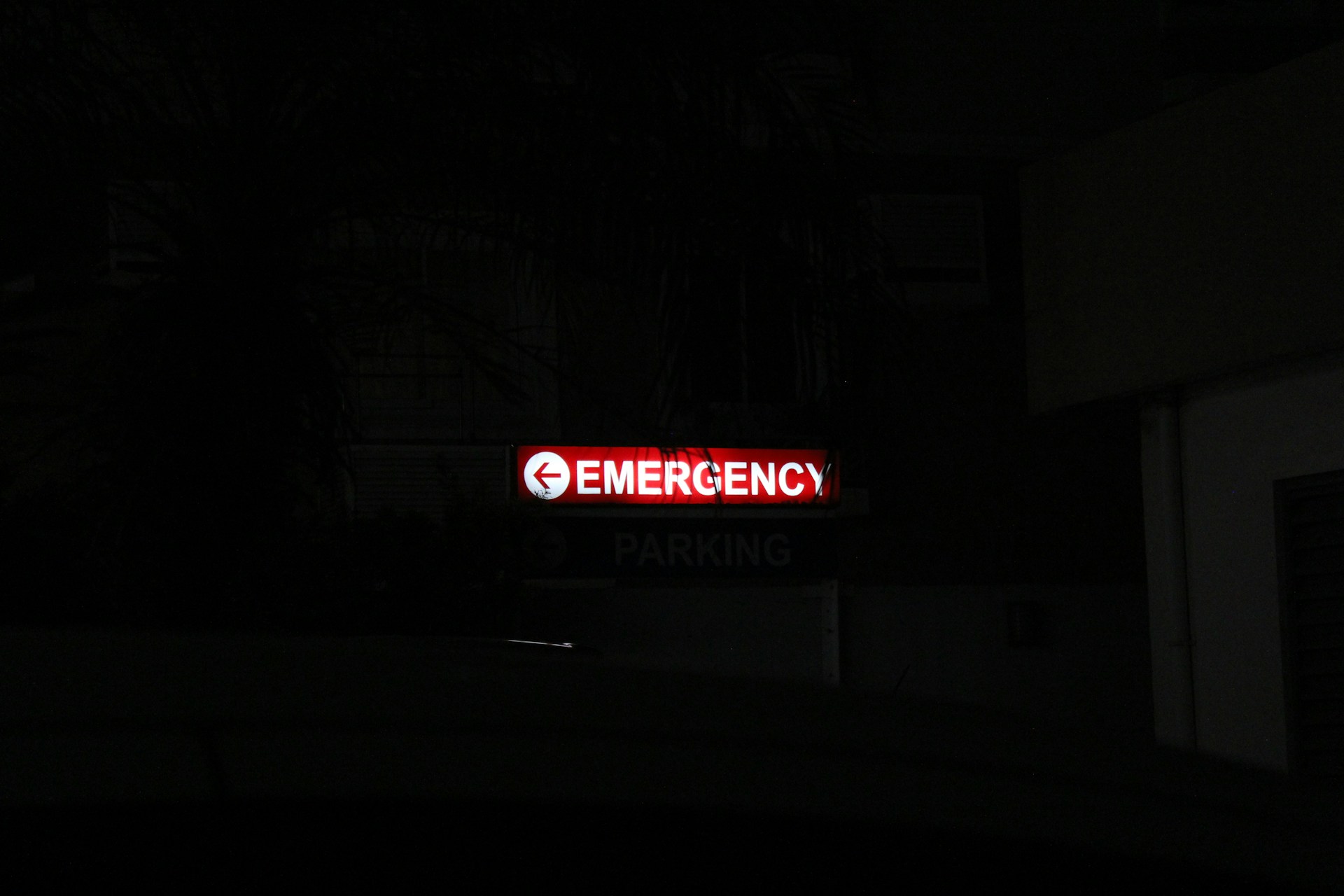 A photo of a red emergency sign behind a black backdrop depicting hospital emergency rooms in Alberta and signficant delays.