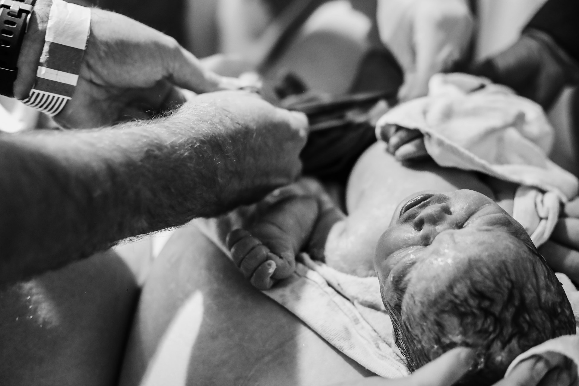 A black and white photo of a new born baby and a person with a hospital bracelet on attending to the newborn baby signalling how delayed c-sections can result in serious birth injuries.