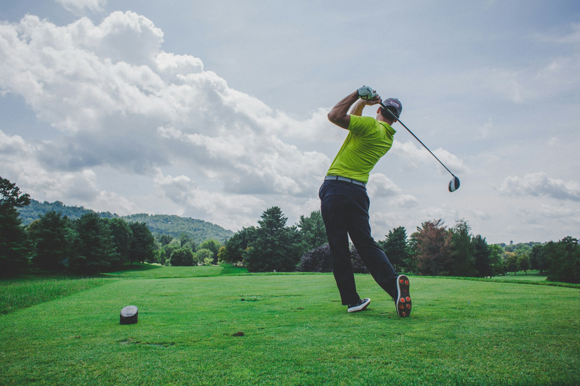 A person in a bright yellow-green shirt on a golf course who just hit the ball and is at the end of the swing.