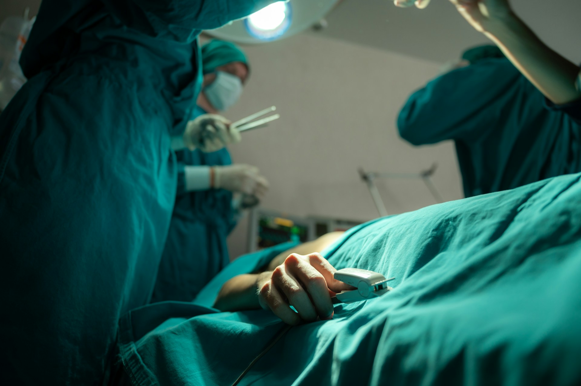 A person lies on an emergency room bed covered in surgical drapes while three doctor in green scrubs and wearing medical masks treat the ptient, representing ER misdiagnosis of brain injuries.