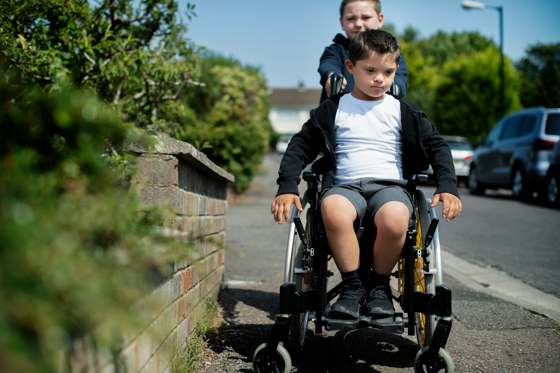 A child pushing another child in a wheelchair down a street that represents cerebral palsy in Alberta.