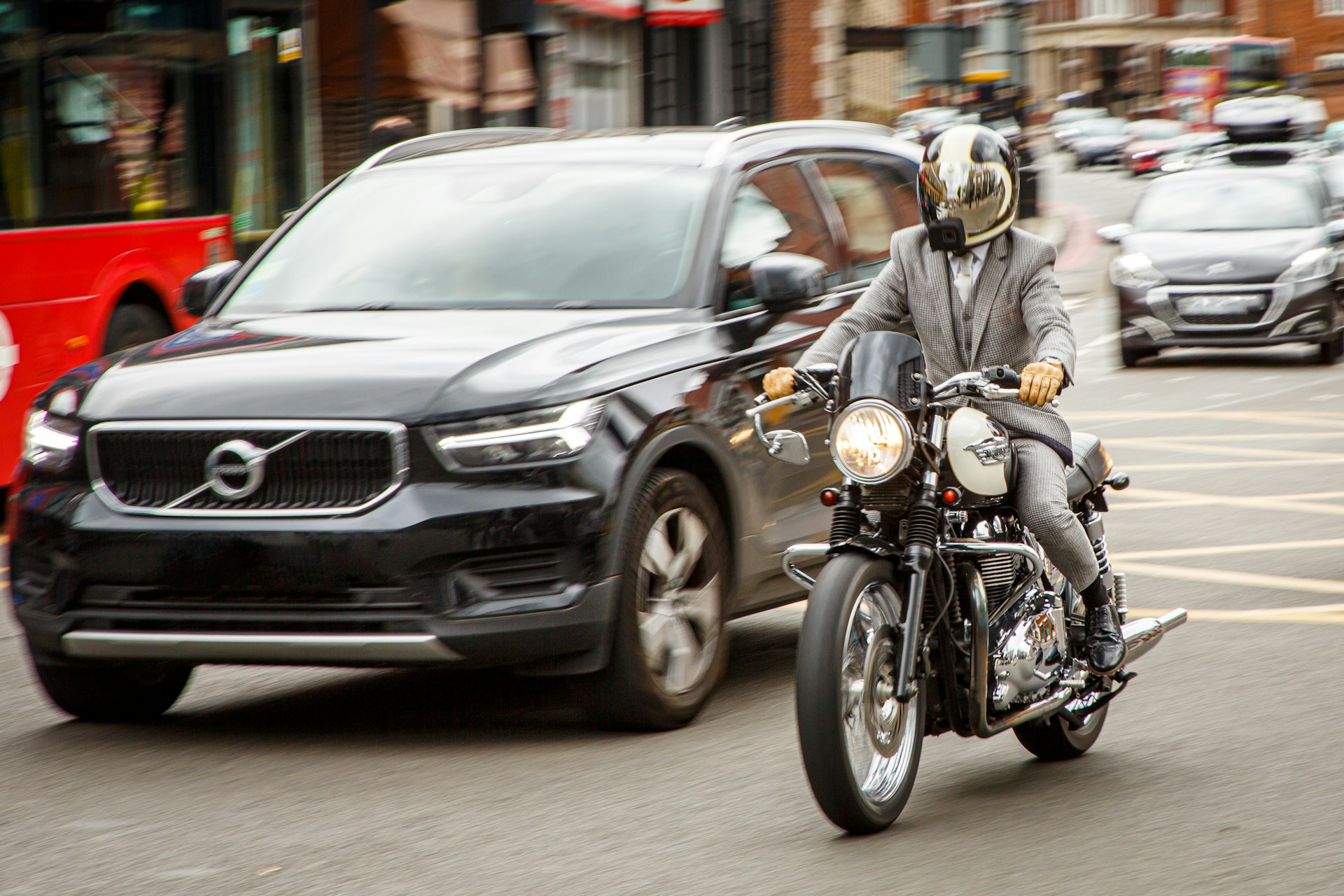 A motorcycle speeds past a black car on a busy city street, representing lane splitting and filtering for motorcycles.