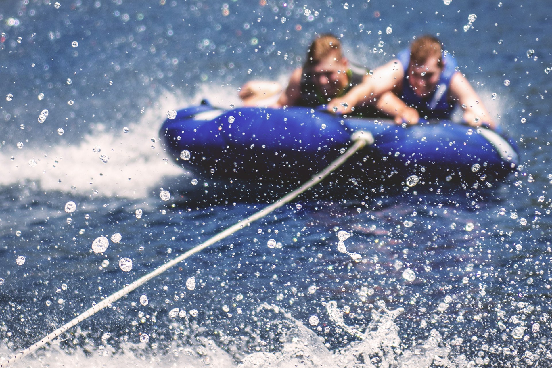 Two boys cling to a blue tube flying over blue water and kicking up droplets of spray, representing towed water sport injuries.