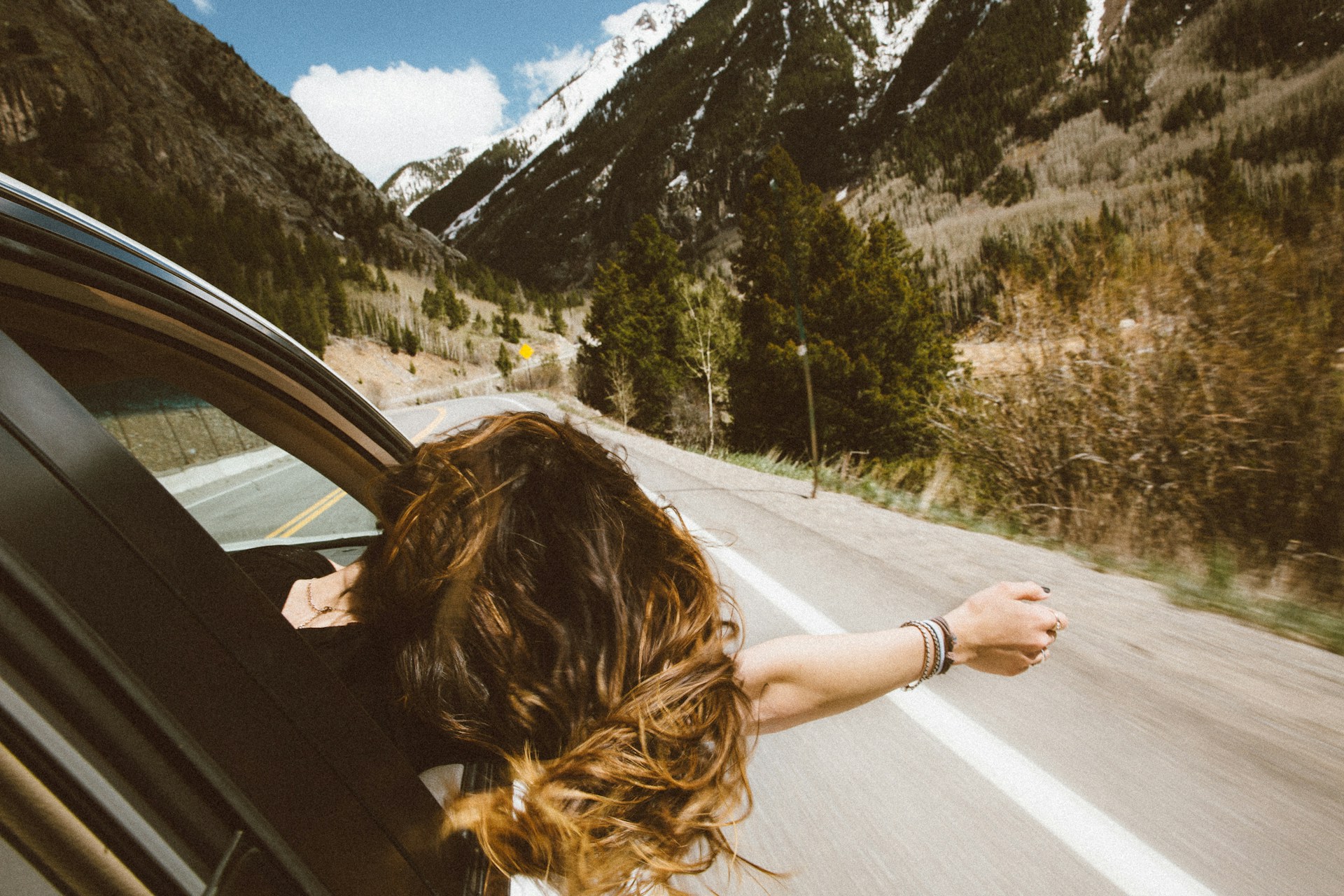 A woman riding in a vehicle putting her hand out the window representing summer recreational accidents in the summertime in Alberta.