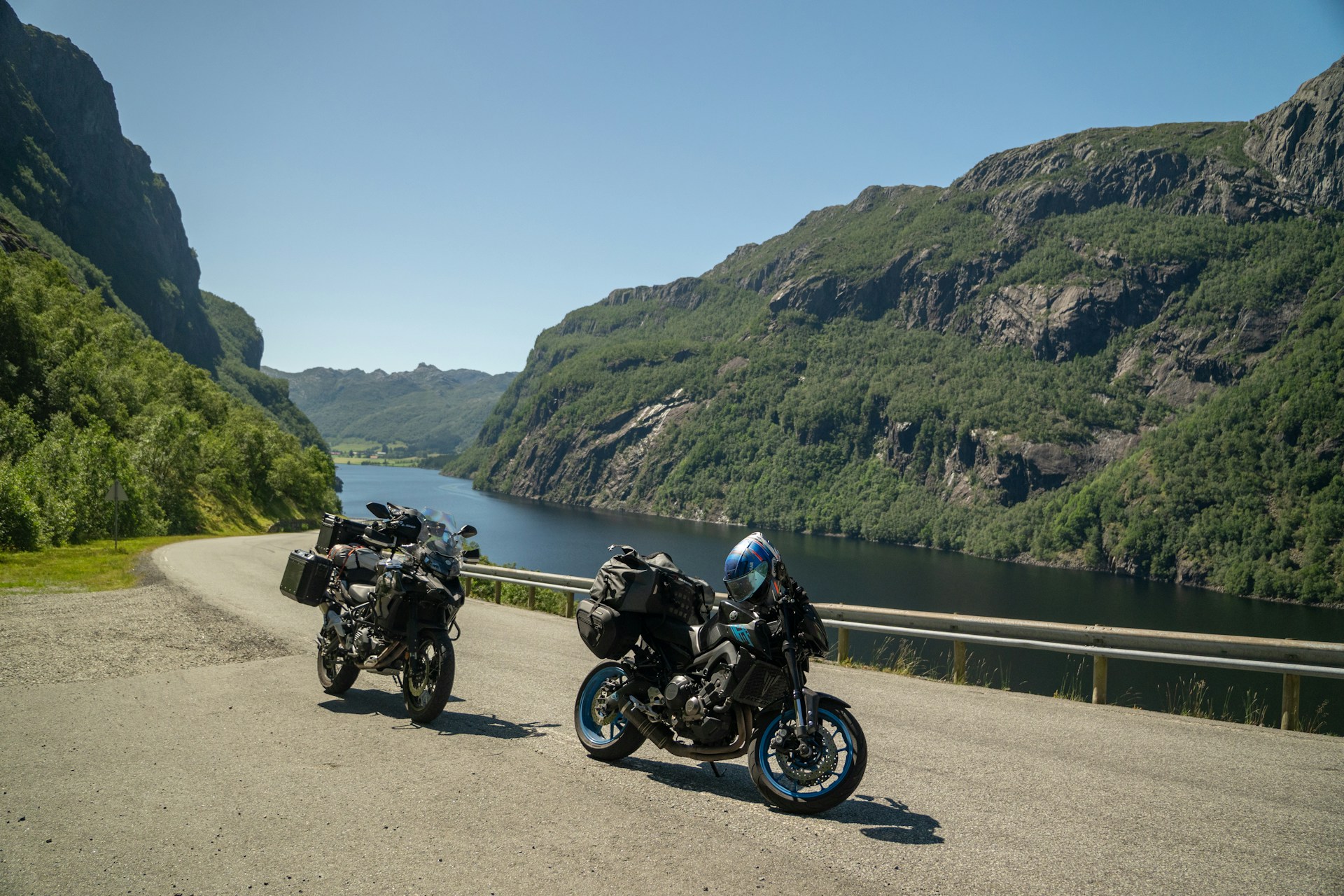Two motorcycles parked at the edge of a narrow road overlooking a river with tree covered ciffs rising uo on either side, representing motorcycle crashes in Alberta.