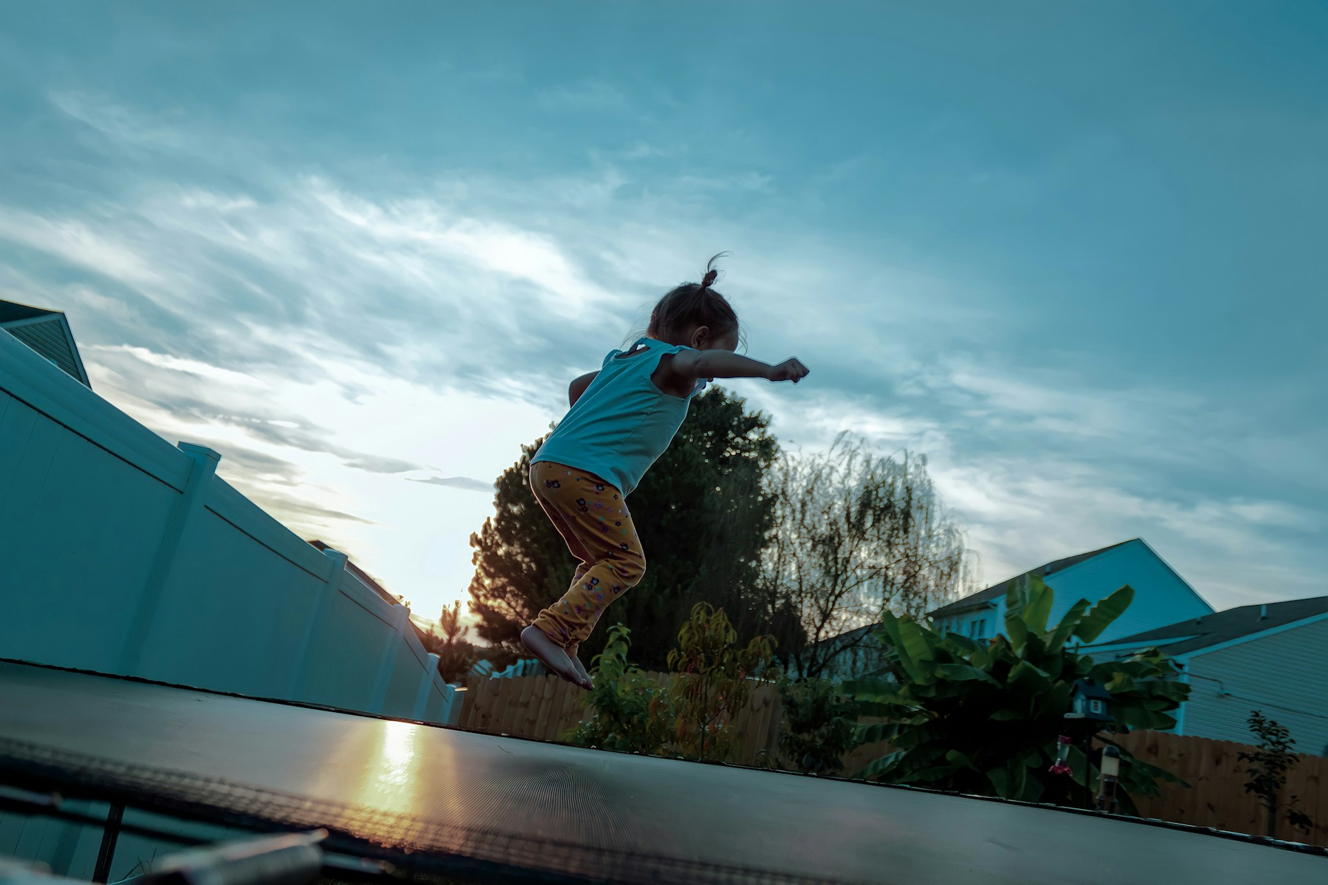 A young girl bounces on a backyard trampoline while the sun sets behind her, representing trampoline accident injuries.